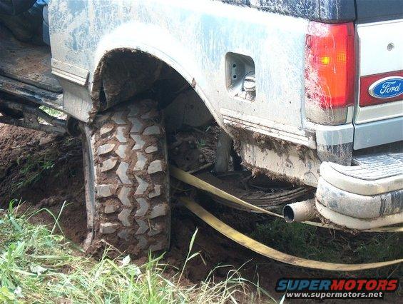 Silver Ford Bronco stuck in mud, rear quarter panel visible with a tow strap around the tire