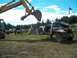 1979 Ford Bronco - An excavator is lifting a heavily modified flatbed pickup truck in an outdoor setting with other vehicles present.