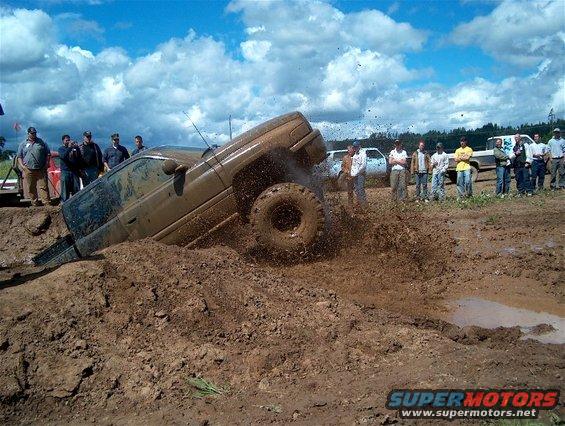 Mud bogging scene with a brown SUV stuck in mud, spectators watching