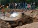 1979 Ford Bronco - A muddy pickup truck is stuck in a mud pit while onlookers watch the event.