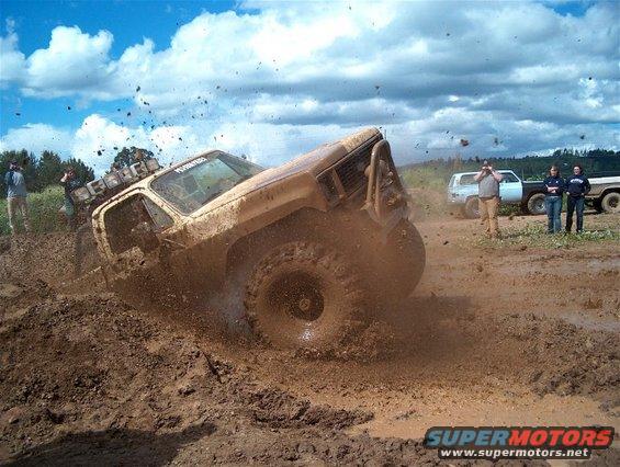 Yellow off-road vehicle splashing mud, with other trucks in background