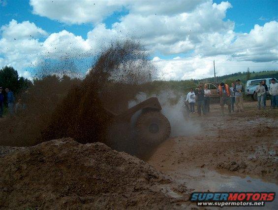 Off-road vehicle kicking up mud in a muddy field with spectators watching
