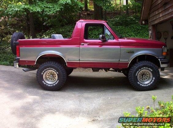 Red and silver Ford Bronco parked outside a garage. Has a spare tire on the back