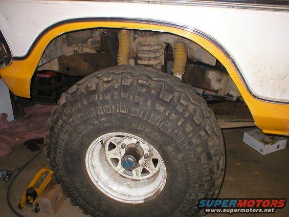 White and yellow vehicle wheel well with large off-road tire and yellow shocks