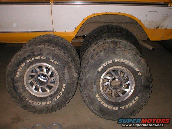 Four Mud King XT steel radial tires stacked next to a white and yellow vehicle