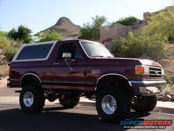 Maroon Ford Bronco with a white top, lifted with large tires, seen from a 3/4 front angle