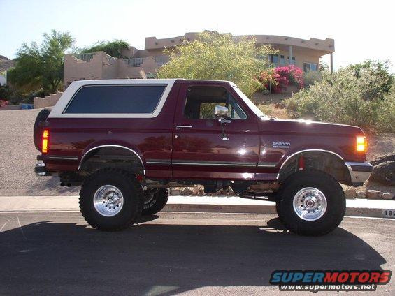 Maroon Ford Bronco with a white top, lifted with large tires, parked outside a house