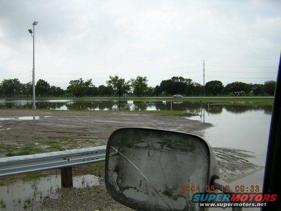 side mirror view of flooded road with a car in distance