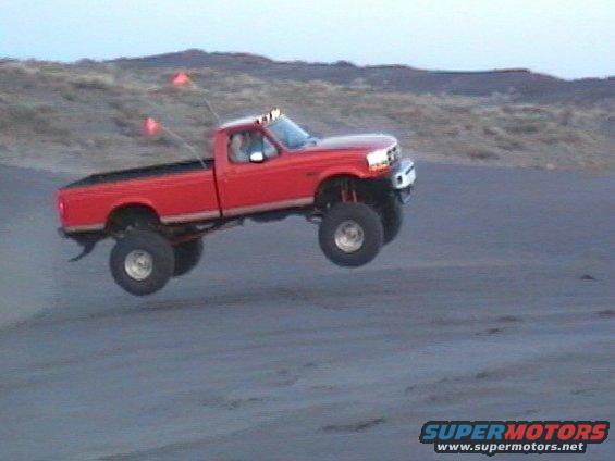 Red 1993 Ford F-350 jumping a dune