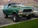 1979 Ford Bronco - This lifted green Ford Bronco is parked in a lot with mountains in the background.