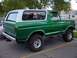 1979 Ford Bronco - A lifted green Ford Bronco with a white hardtop is parked in a lot, showing its side and rear profile.