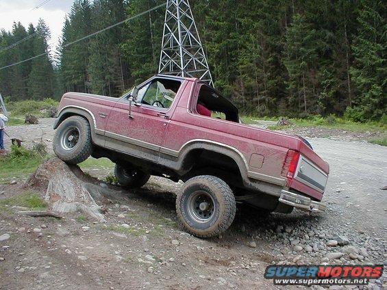 Red SUV with a removable top, driving off-road on a dirt path with rocks and a tree stump