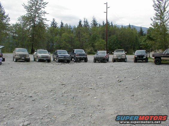 Line of pickup trucks and SUVs parked on gravel