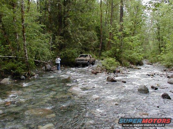 Brown pickup truck crossing stream, forest setting