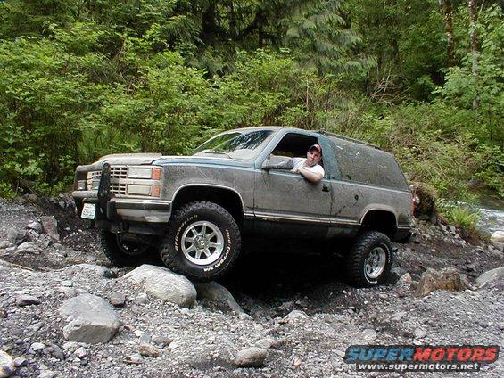 Gray SUV with brush guard navigating a rocky trail, driver visible
