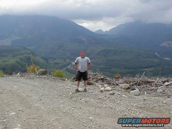 Person standing on a dirt road with mountains in the background