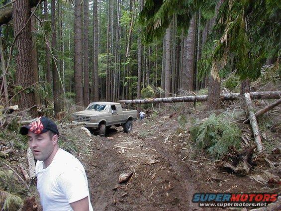 Tan Ford F-Series truck with lifted suspension on a muddy forest road