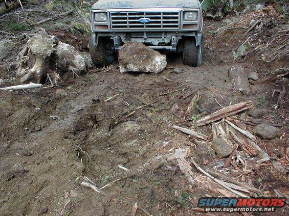 1983 Ford Bronco front grille stuck on a rock in muddy terrain