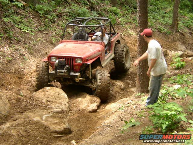 Red off-road vehicle with a roll cage navigating a rocky trail