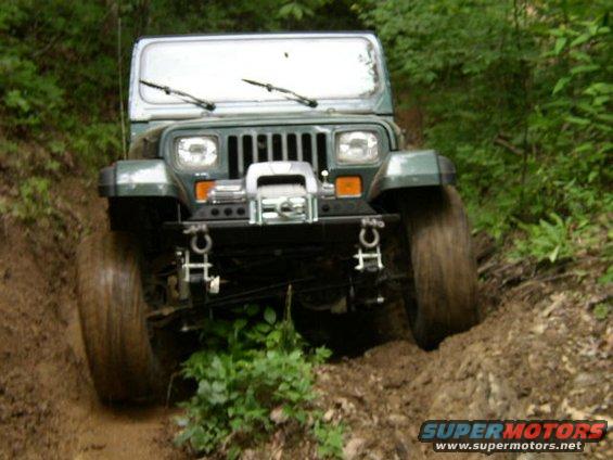 Green Jeep Wrangler on a muddy trail, front view with winch
