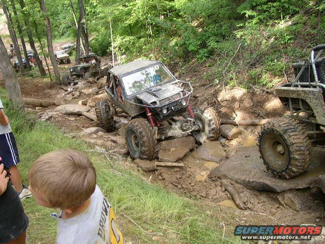 off-road buggy navigating a rocky, muddy trail with other vehicles in the background