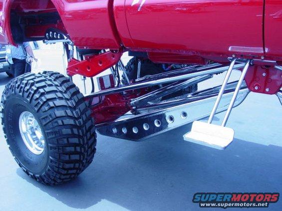 Close-up of a lifted truck's red frame, chrome suspension components, and large off-road tire