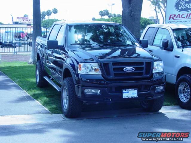 Black Ford F-150 truck, front 3/4 view, parked on grass next to a white truck