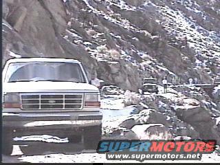 White SUV parked on a snowy mountain road with another vehicle in the distance