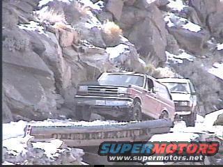 Red 1992 Ford Bronco driving on a rocky, snowy path
