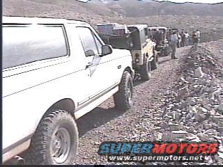 White SUV leads a line of off-road vehicles on a dirt road