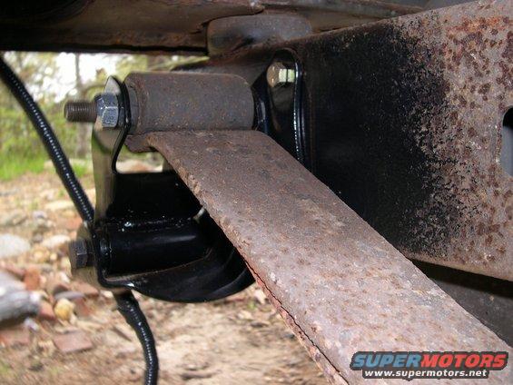 Leaf spring with rust and cracks attached to black suspension bracket with bolt