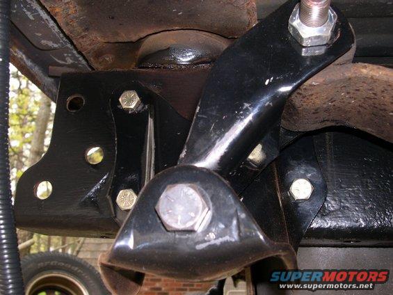 Black suspension bracket with large bolts, tire visible below