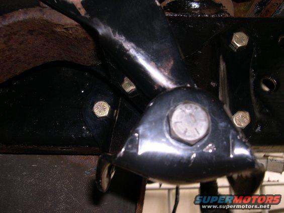 Close-up of black painted vehicle frame brackets and bolts, with rust visible on surrounding metal