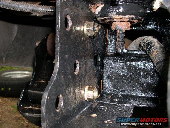 Close-up of black painted vehicle frame with bolts and suspension parts. A tire is visible in the background