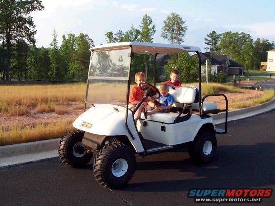 White golf cart with three children driving on a paved road