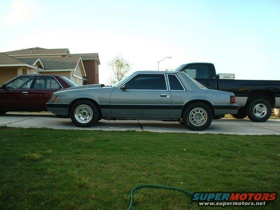 1982 Ford Mustang coupe parked next to a maroon sedan and a black pickup truck