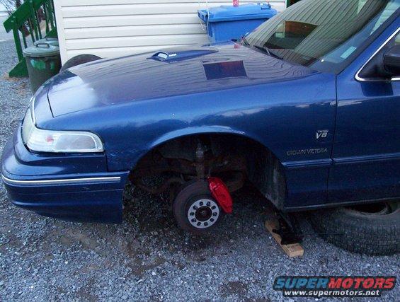 Blue 1995 Ford Crown Victoria, front quarter view, missing front wheel, red brake caliper visible