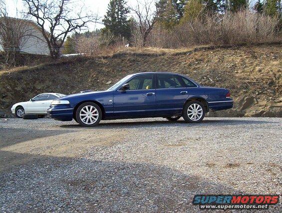Blue 1995 Ford Crown Victoria sedan, side view. Another white car is parked behind it