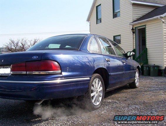 Blue 1995 Ford Crown Victoria sedan, rear quarter view, with exhaust smoke