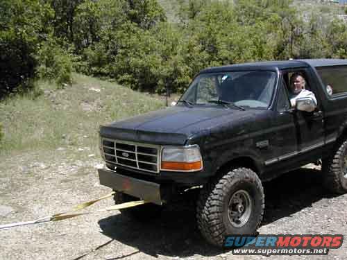 Black Ford Bronco with a tow strap attached to the front bumper, driver visible