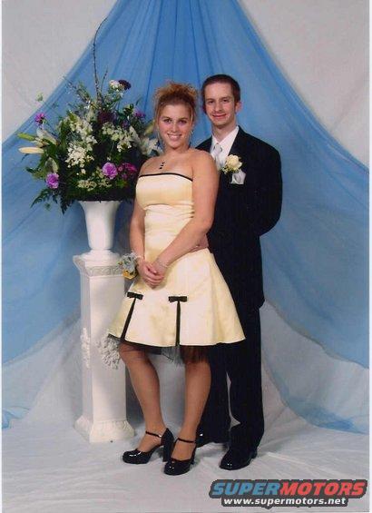 Young couple in formal wear posing for a photo in front of a blue drape and floral arrangement