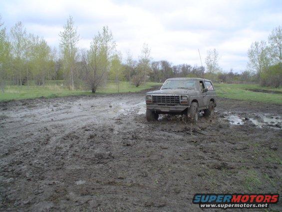 Mud-splattered gray Ford Bronco driving through a muddy field