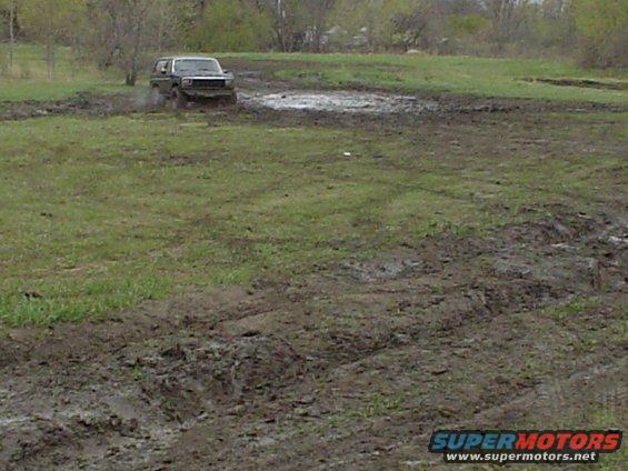 SUV driving through a muddy field, kicking up water