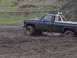 1981 Ford Bronco - A dark-colored pickup truck navigates a muddy terrain, kicking up water and dirt.