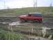 1981 Ford Bronco - Red Chevrolet K5 Blazer navigating a muddy off-road course.