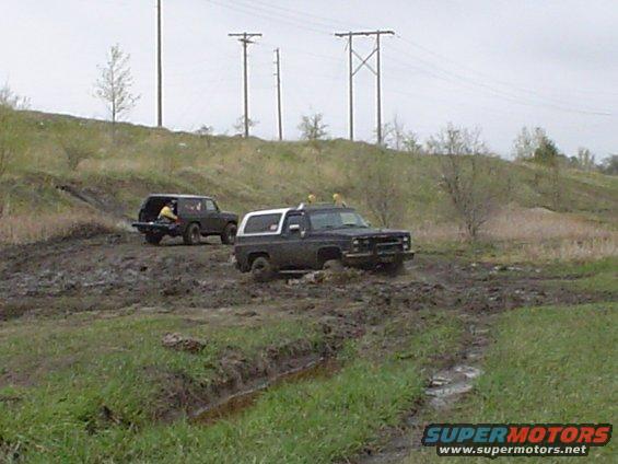 Two SUVs driving through a muddy field with power lines overhead