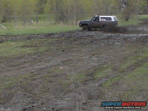 Dark SUV with white top driving through mud. 1981 Ford Bronco