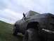 1981 Ford Bronco - Mud-covered pickup truck on a grassy slope under an overcast sky.