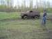 1981 Ford Bronco - A red SUV is stuck in the mud, with two people inside and one person standing nearby.