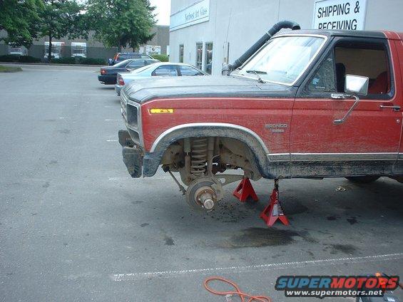 1983 Ford Bronco front end raised on red jack stands, front wheel removed